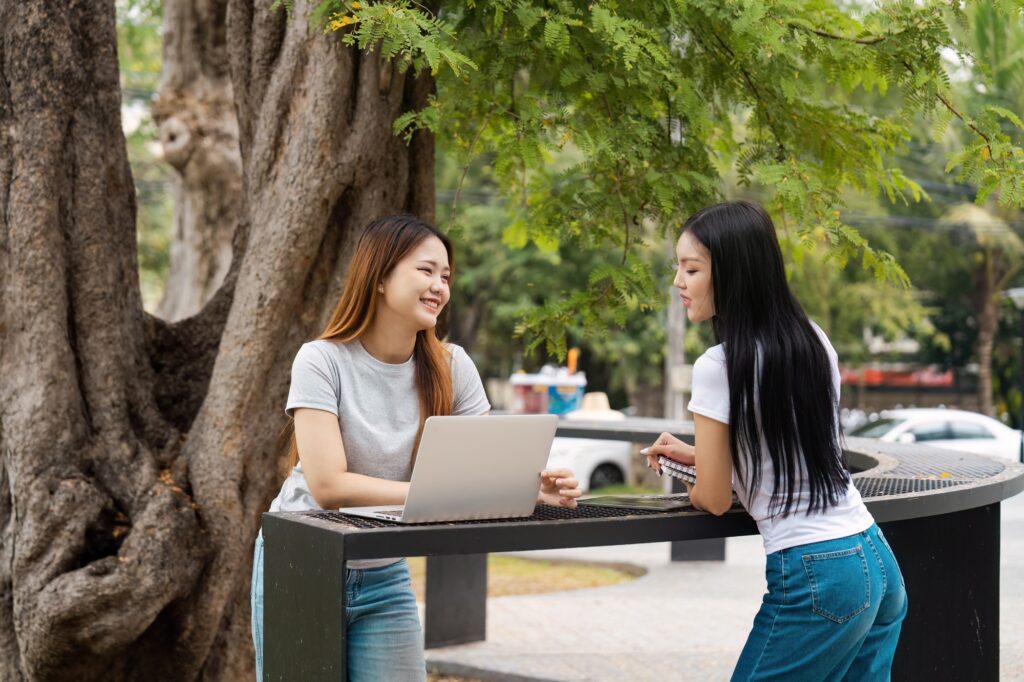Diverse female students discussing study material outdoors by a tree.